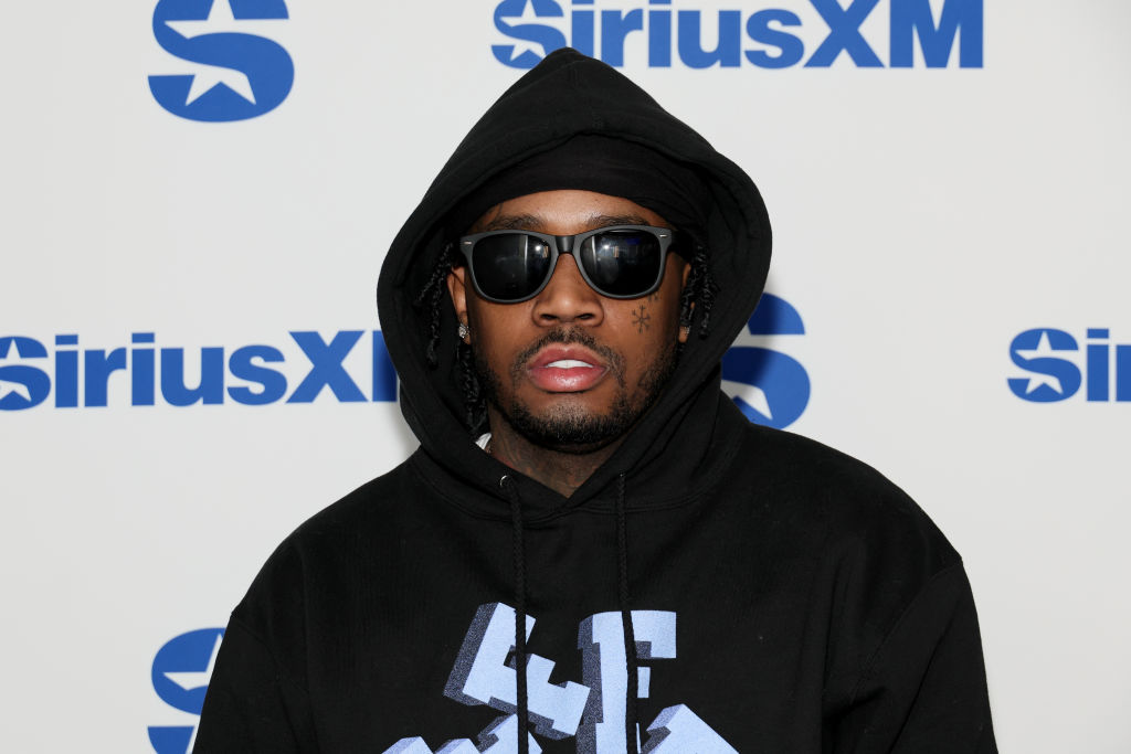 A man wearing sunglasses and a black hoodie stands in front of a SiriusXM backdrop.