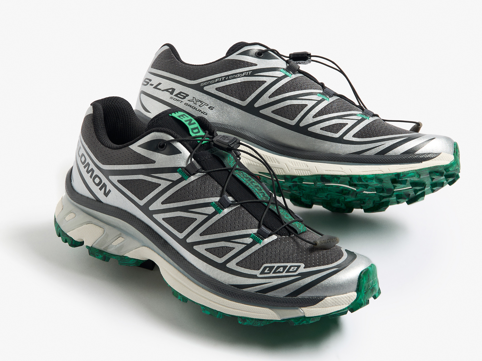 A pair of Salomon S-Lab XT-6 sneakers in black, gray, and green with a rugged design and distinctive lacing system.