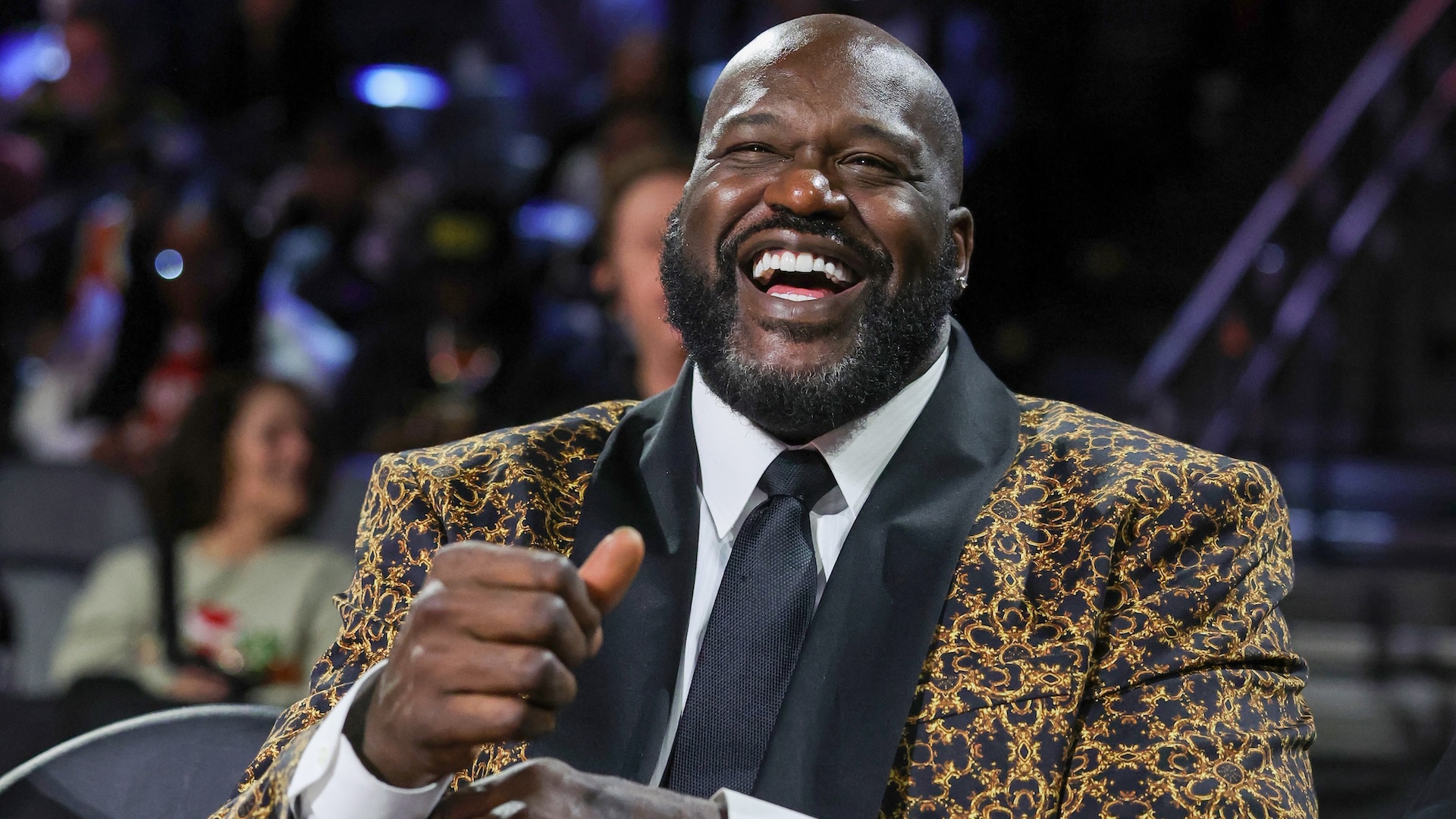 Shaquille O'Neal, wearing a patterned suit jacket, laughs heartily at an event.