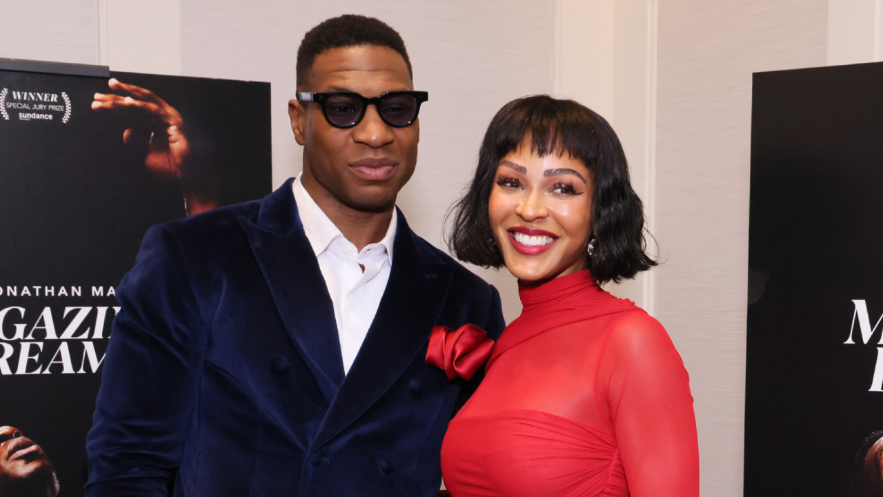 Jonathan Majors wearing sunglasses and a blue suit, and tMeagan Good in a red dress.