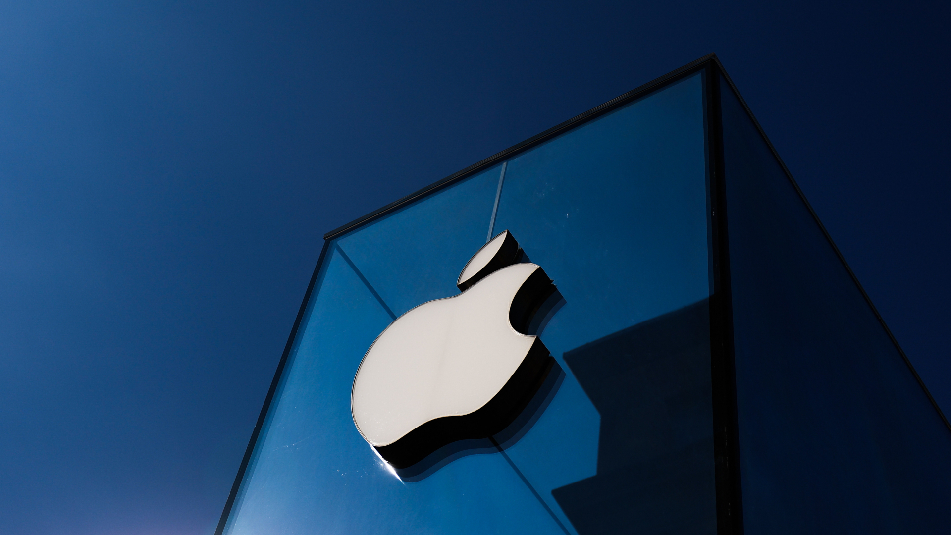 Apple logo on a glass building against a clear blue sky.