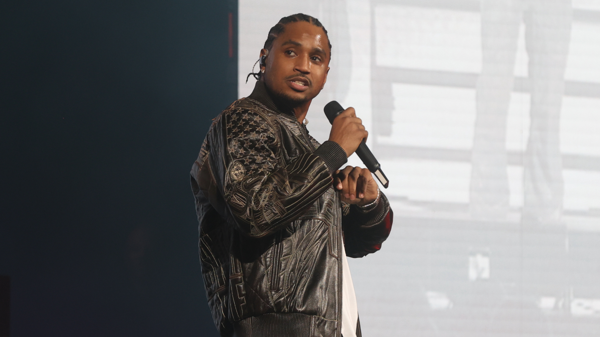 Trey Songz on stage holding a microphone, wearing a patterned leather jacket.