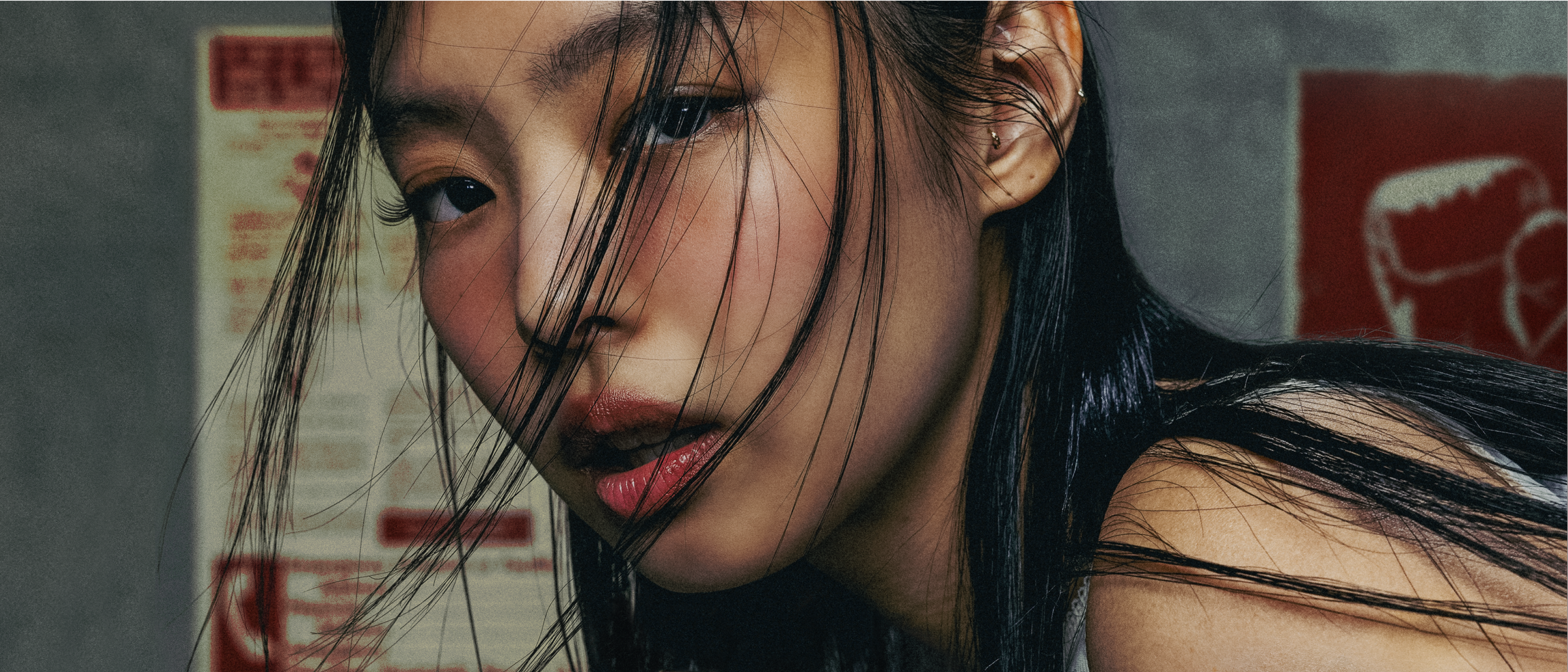 A person with long black hair and wind-swept strands, looking intently at the camera. The background has posters with red text. jennie complex cover