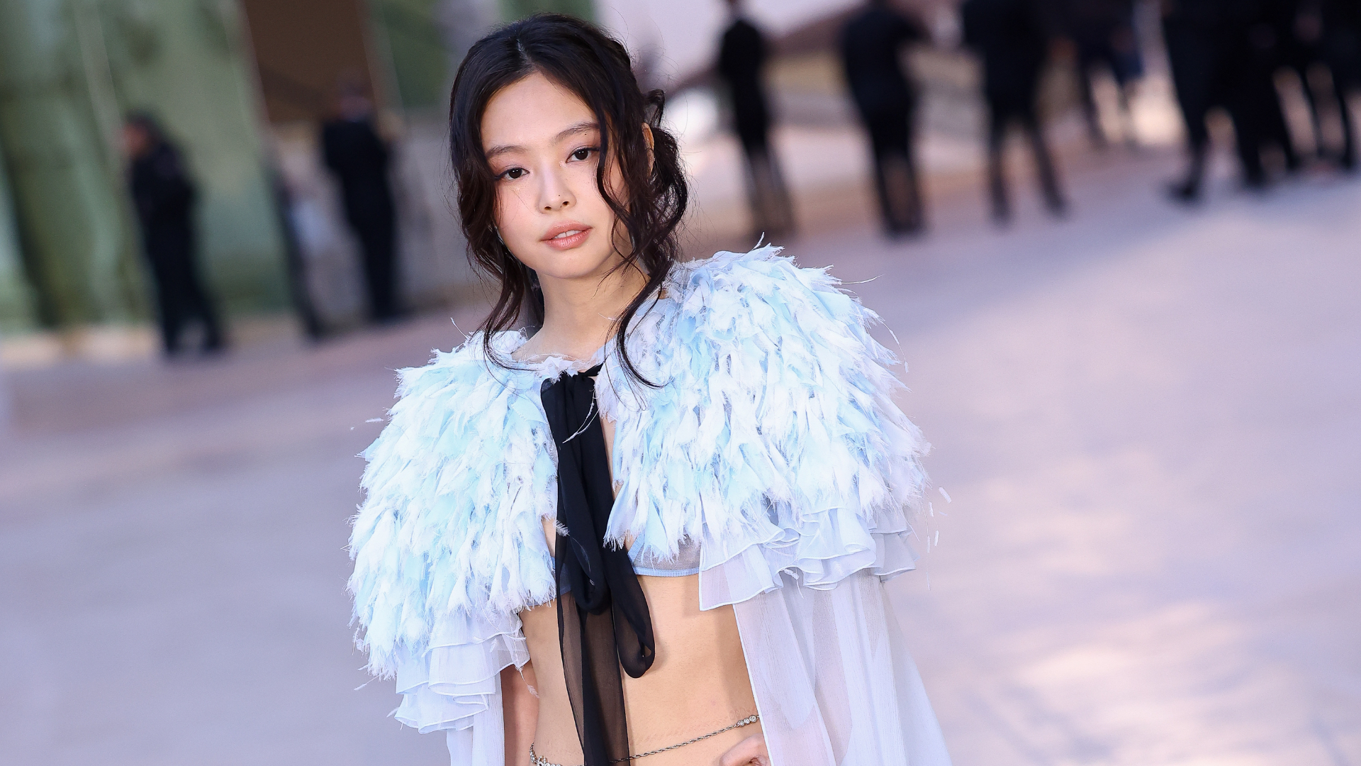 Jennie from BLACKPINK in a feathered outfit, posing at an event.