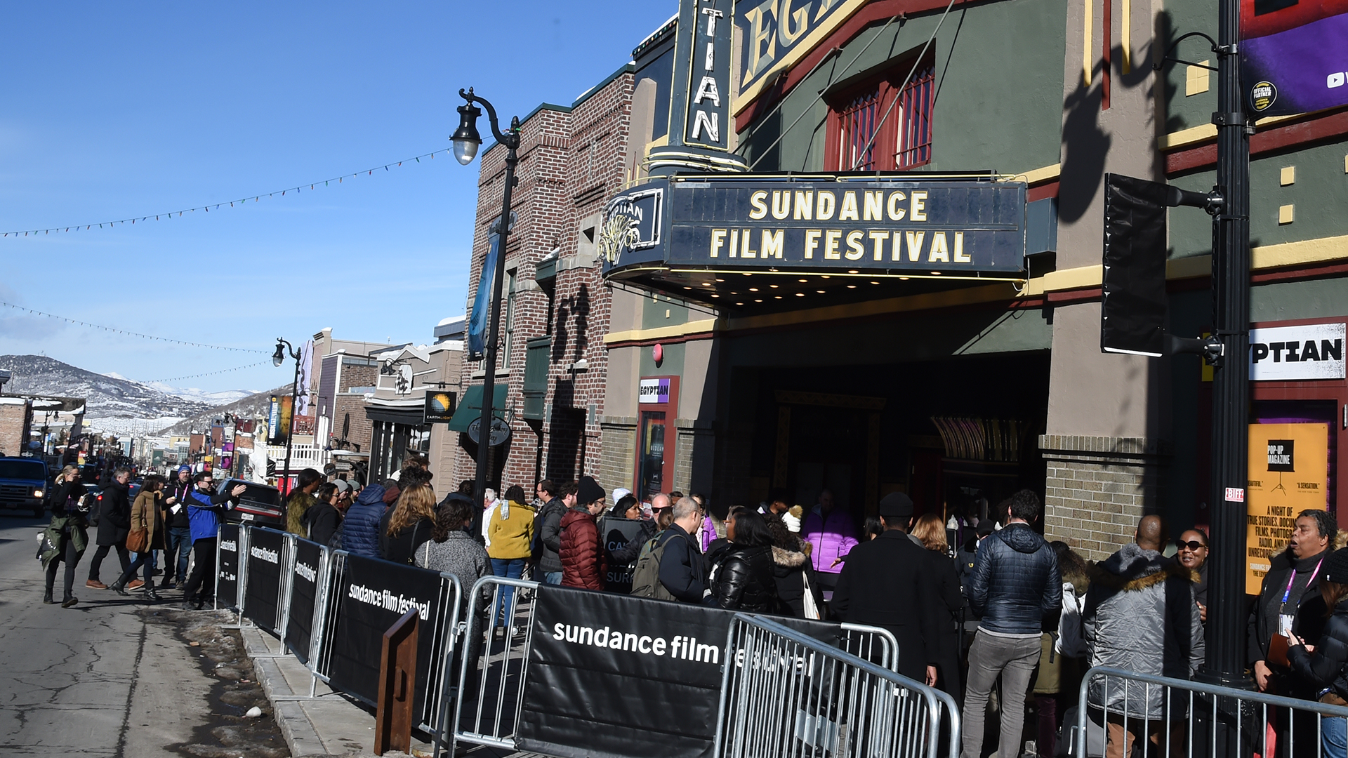 Crowd outside the Egyptian Theatre at the Sundance Film Festival. People are lined up along barriers on a sunny day.