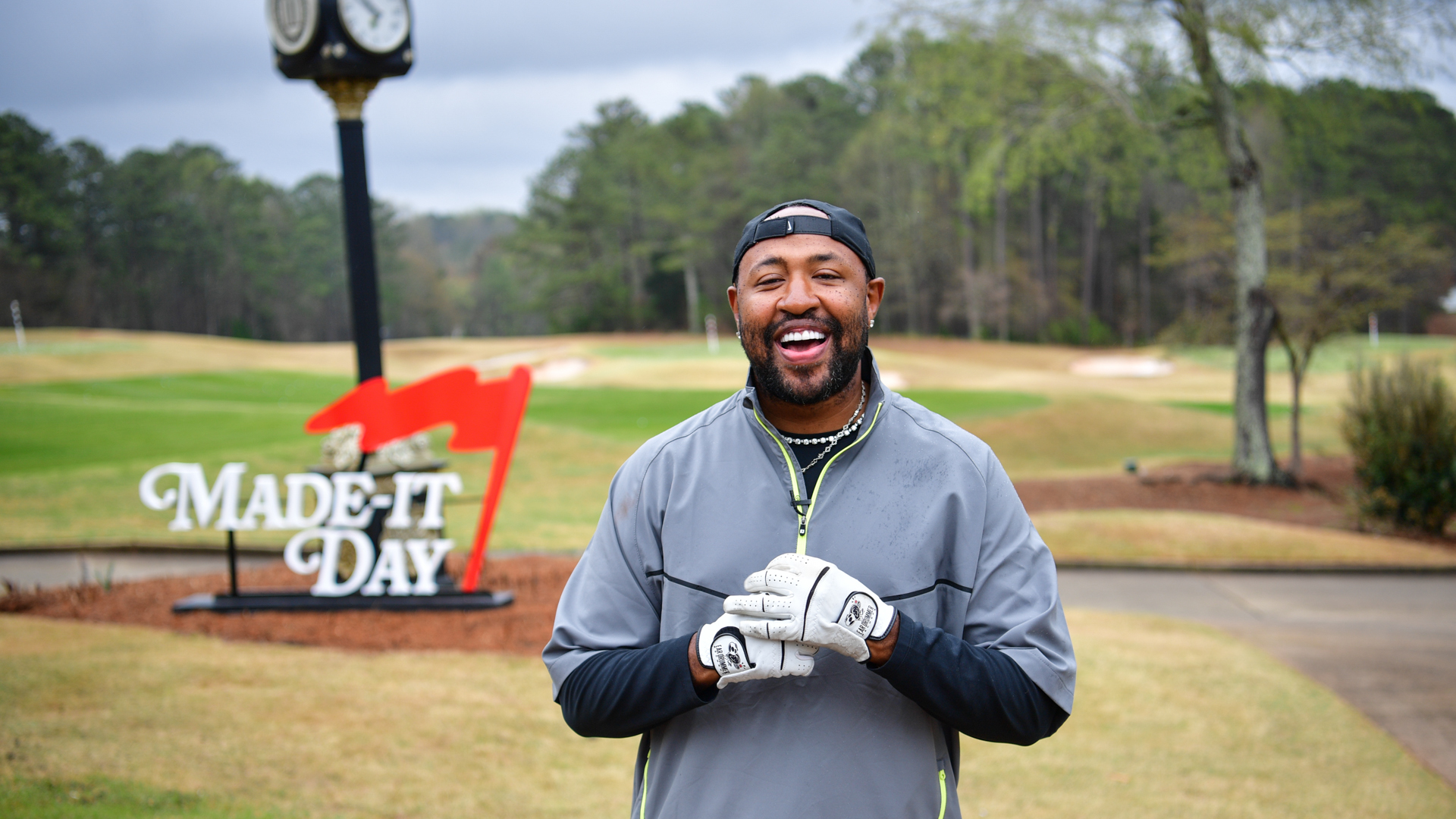 Mike Will Made-It in a golf outfit smiling on a golf course with a "Made-It Day" sign and clock in the background.