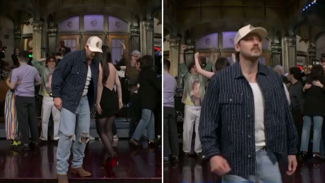 Morgan Wallen in a cap and casual outfit stands on stage at 'Saturday Night Live' in front of people in the background.