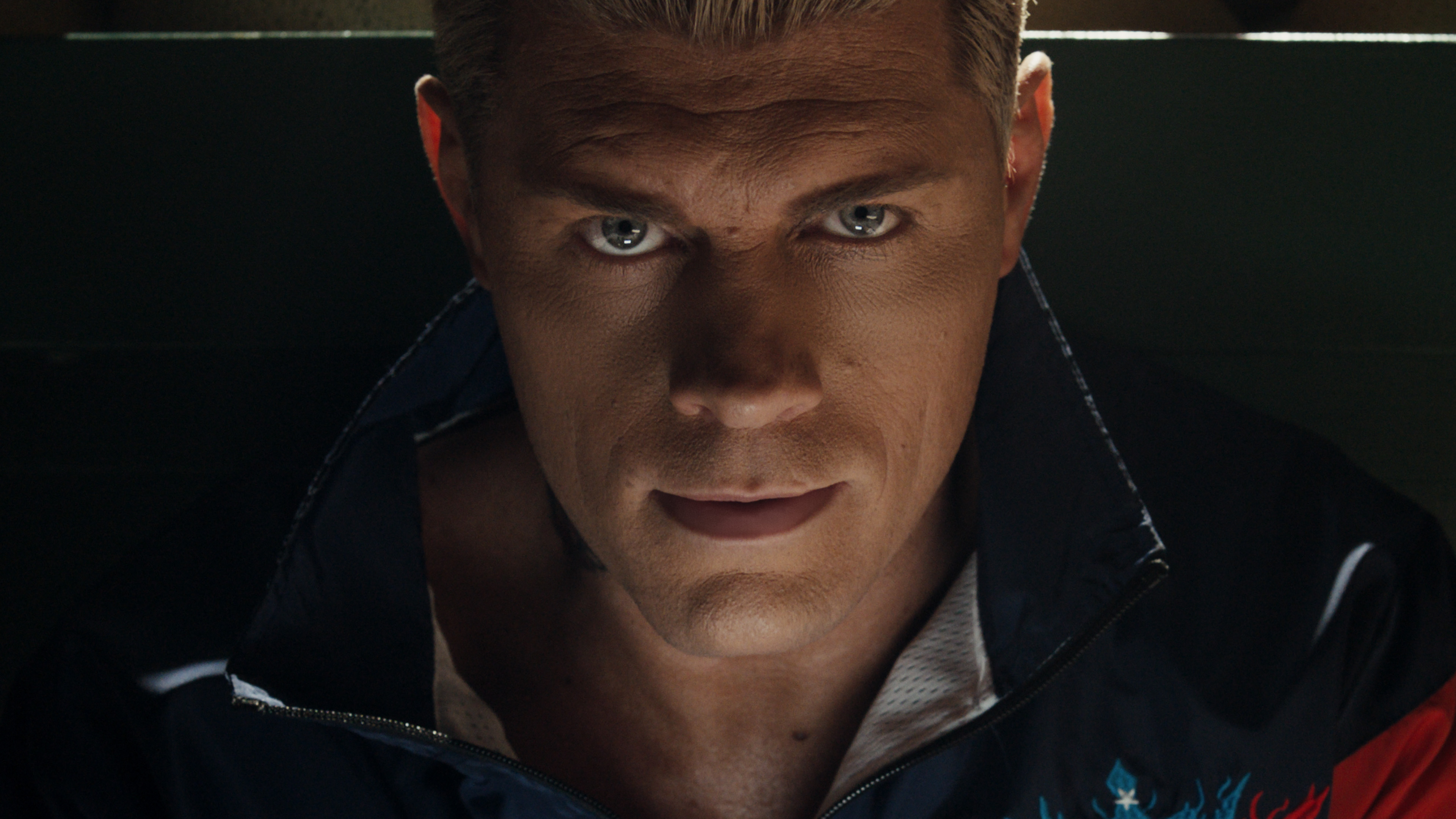 Cody Rhodes with short, light-colored hair and intense expression, wearing a dark jacket with a hint of a white shirt underneath.