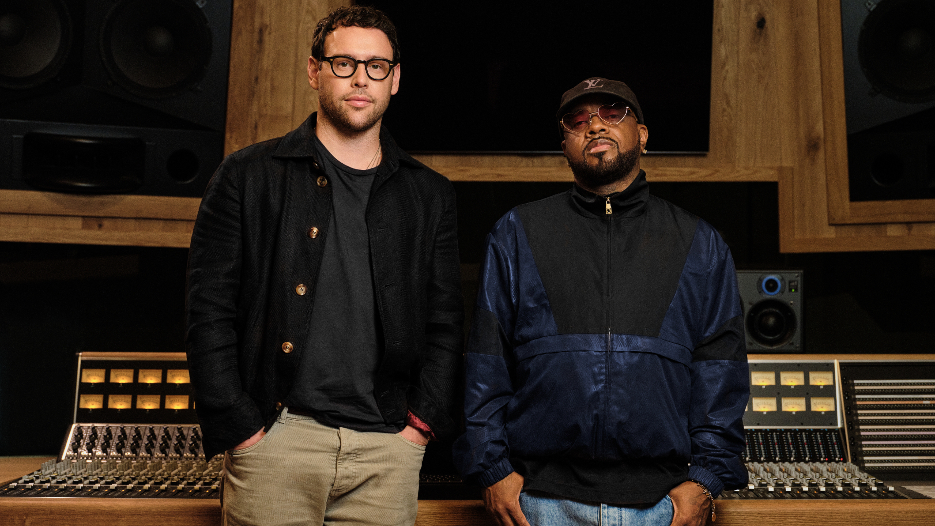 Scooter Braun and Jermaine Dupri standing in a recording studio, one wearing glasses and a black jacket, the other in a cap and navy jacket.