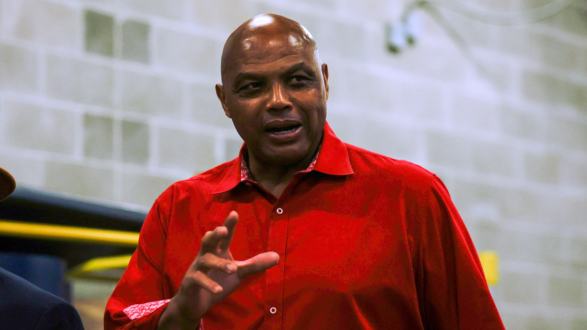 Charles Barkley, wearing a red shirt, gestures while speaking indoors.