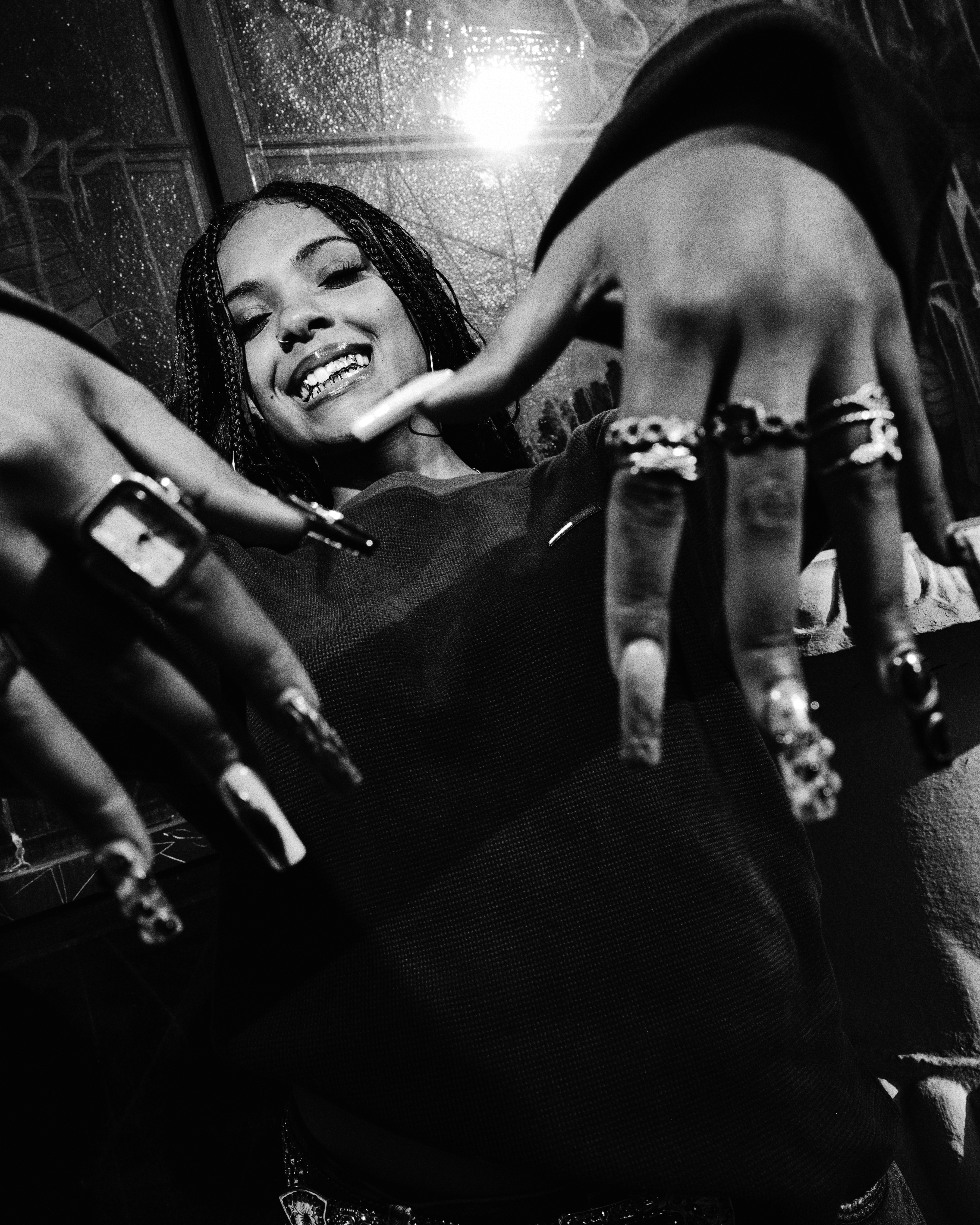 Samara Cyn smiling with braided hair, showcasing rings and long nails in a black and white photo.