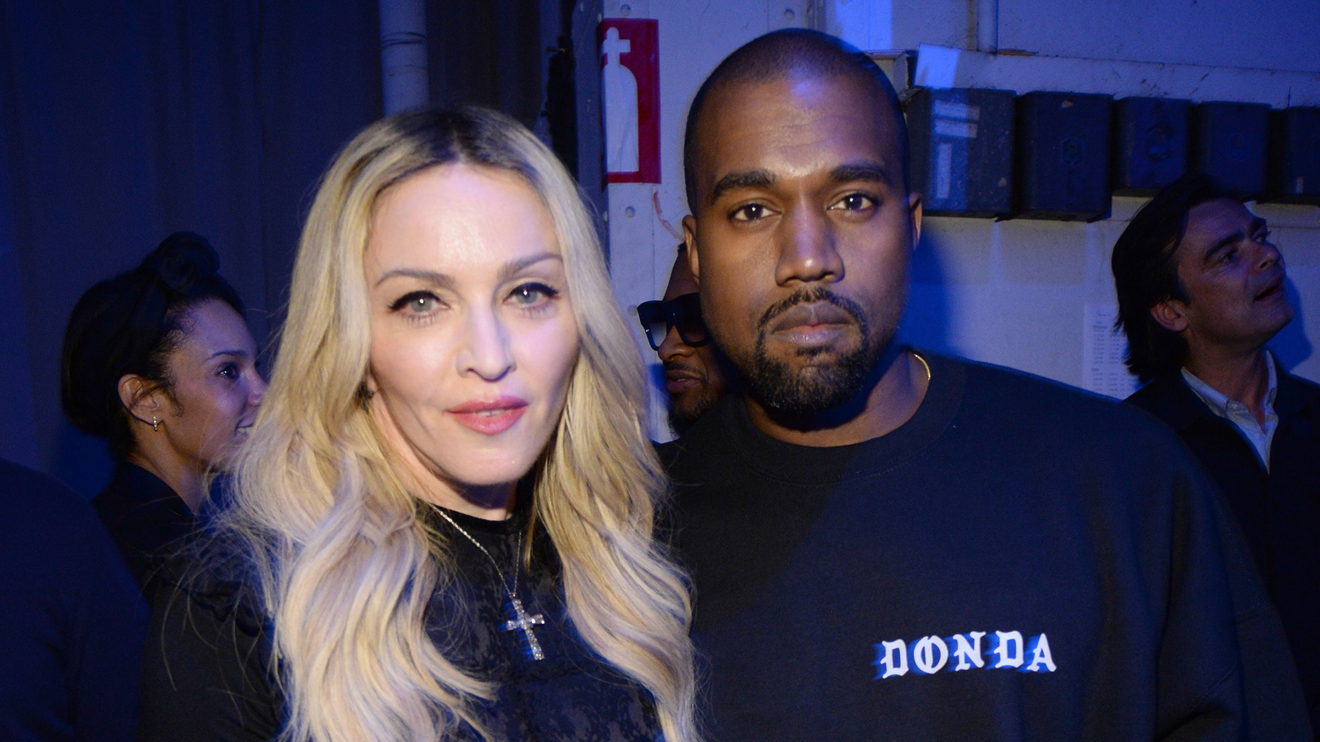 Madonna and Kanye West pose together. Madonna has long blonde hair, and Kanye wears a black "Donda" sweatshirt.
