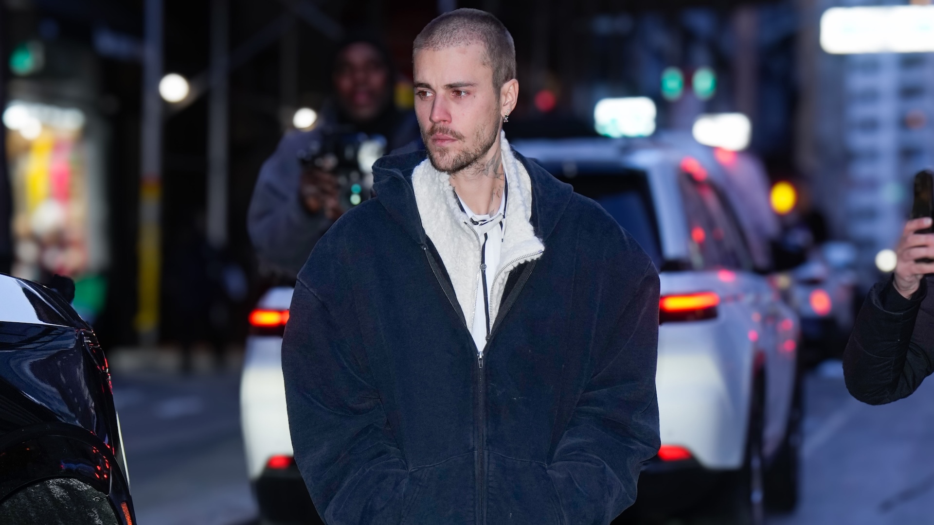 Justin Bieber walking down a street wearing a blue hoodie.