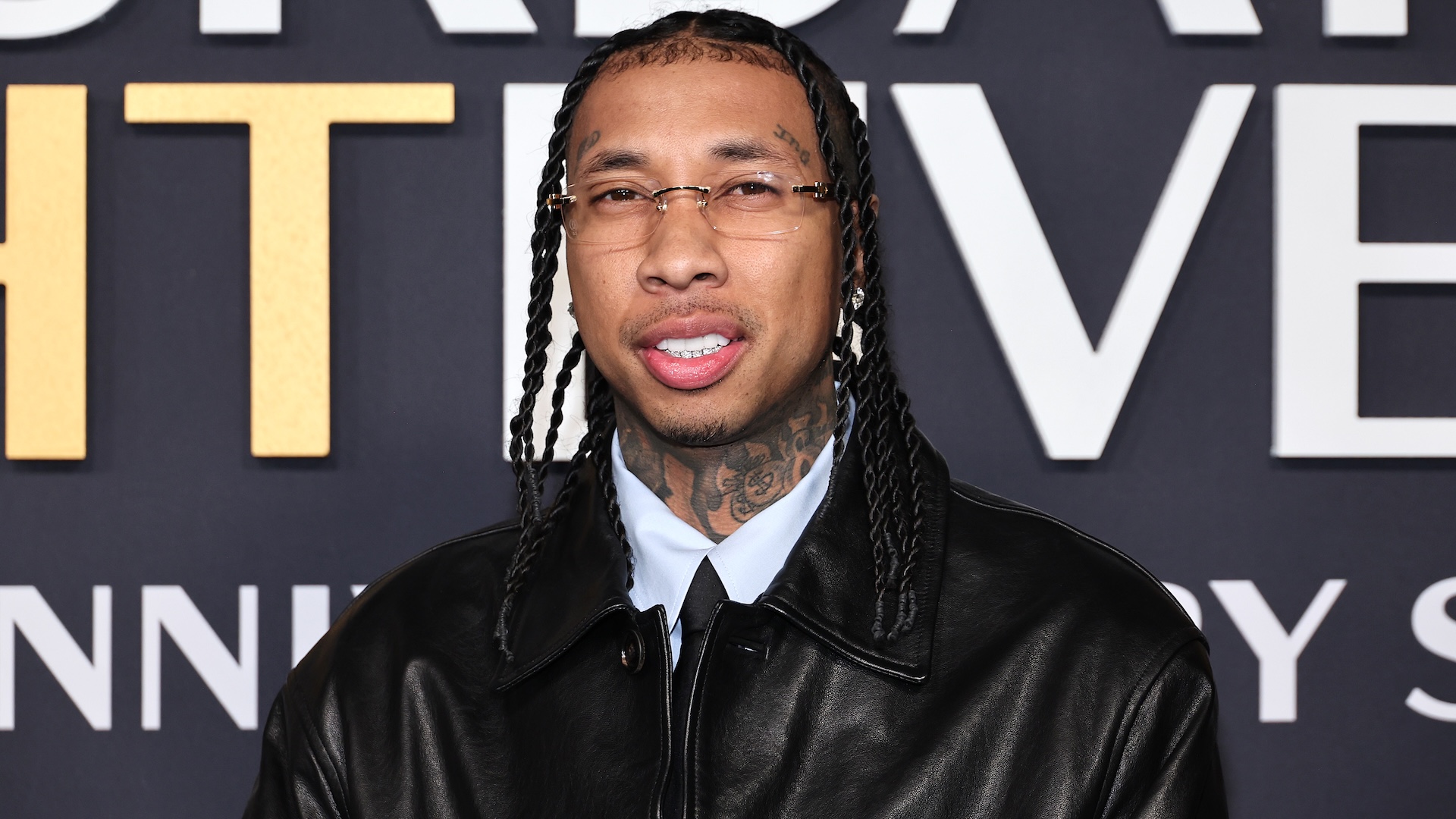 Tyga sports a black leather jacket and glasses.