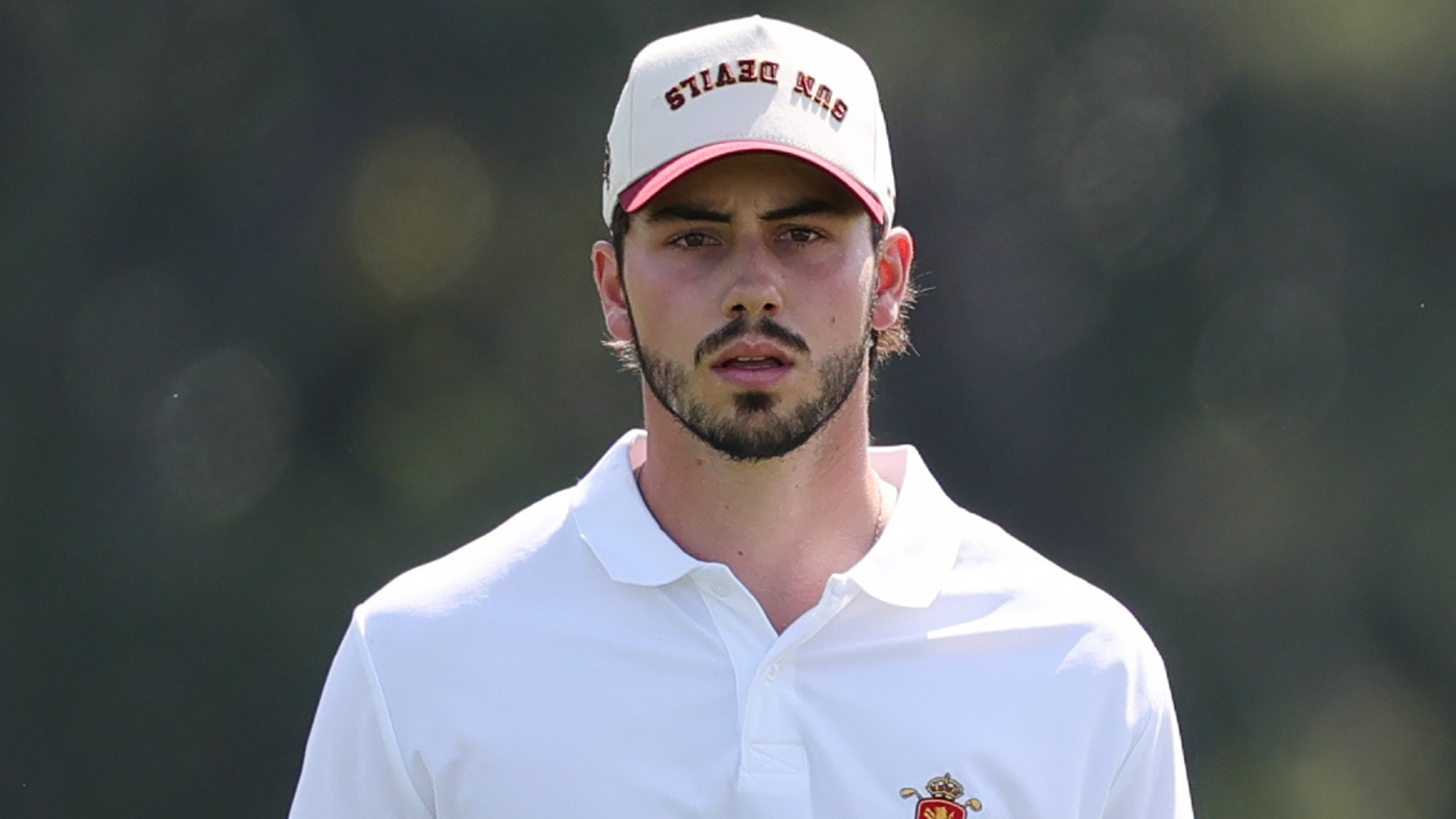 A man in a white polo shirt and a cap, outdoors.