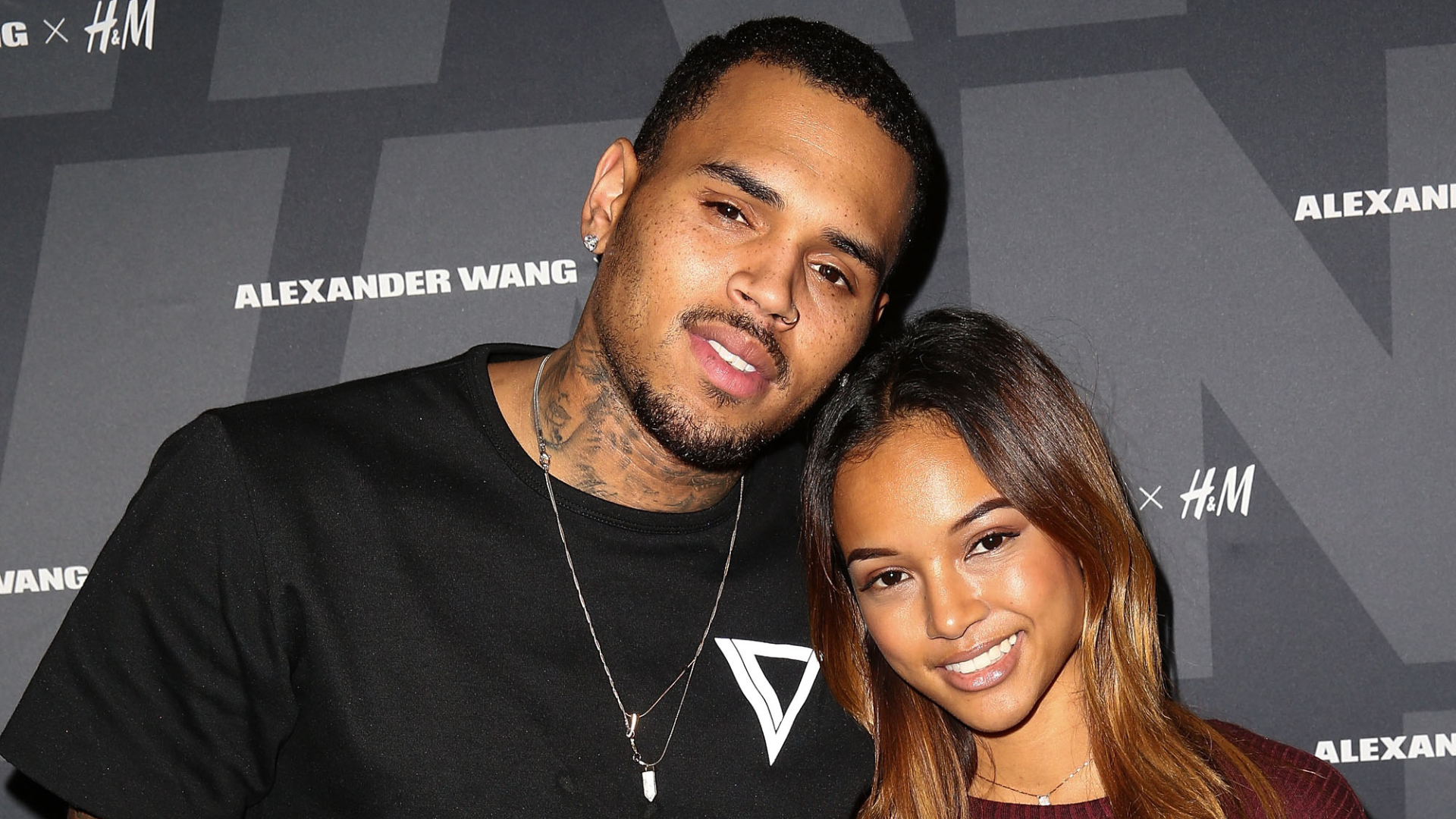 Chris Brown and Karrueche Tran posing together at an event, with an Alexander Wang x H&M backdrop.