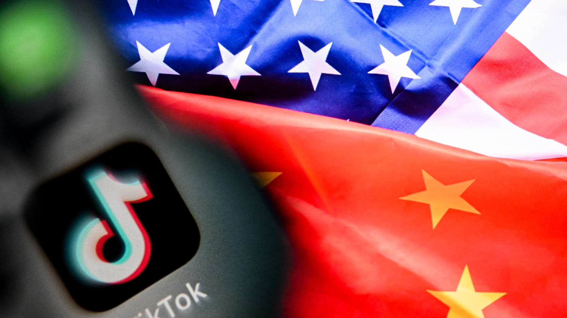 TikTok logo on a smartphone screen, with overlapping American and Chinese flags in the background.