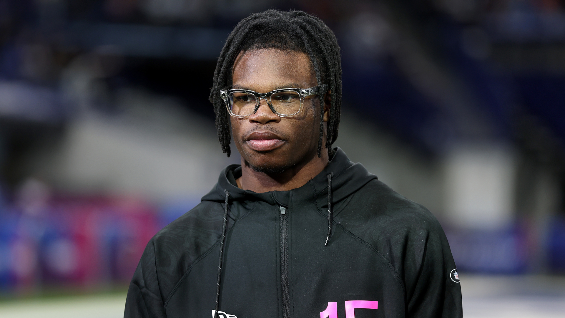 A person wearing glasses and a black hoodie with the number 15, standing indoors with a blurred background.