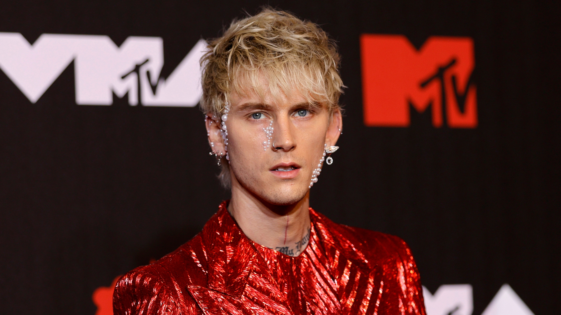 Machine Gun Kelly in a red sequined outfit with facial jewelry at the MTV event.