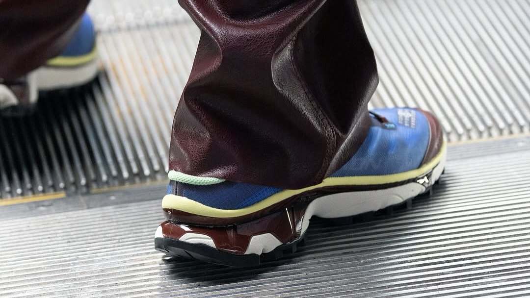 Close-up of a person wearing blue and white sneakers with maroon pants, standing on an escalator.