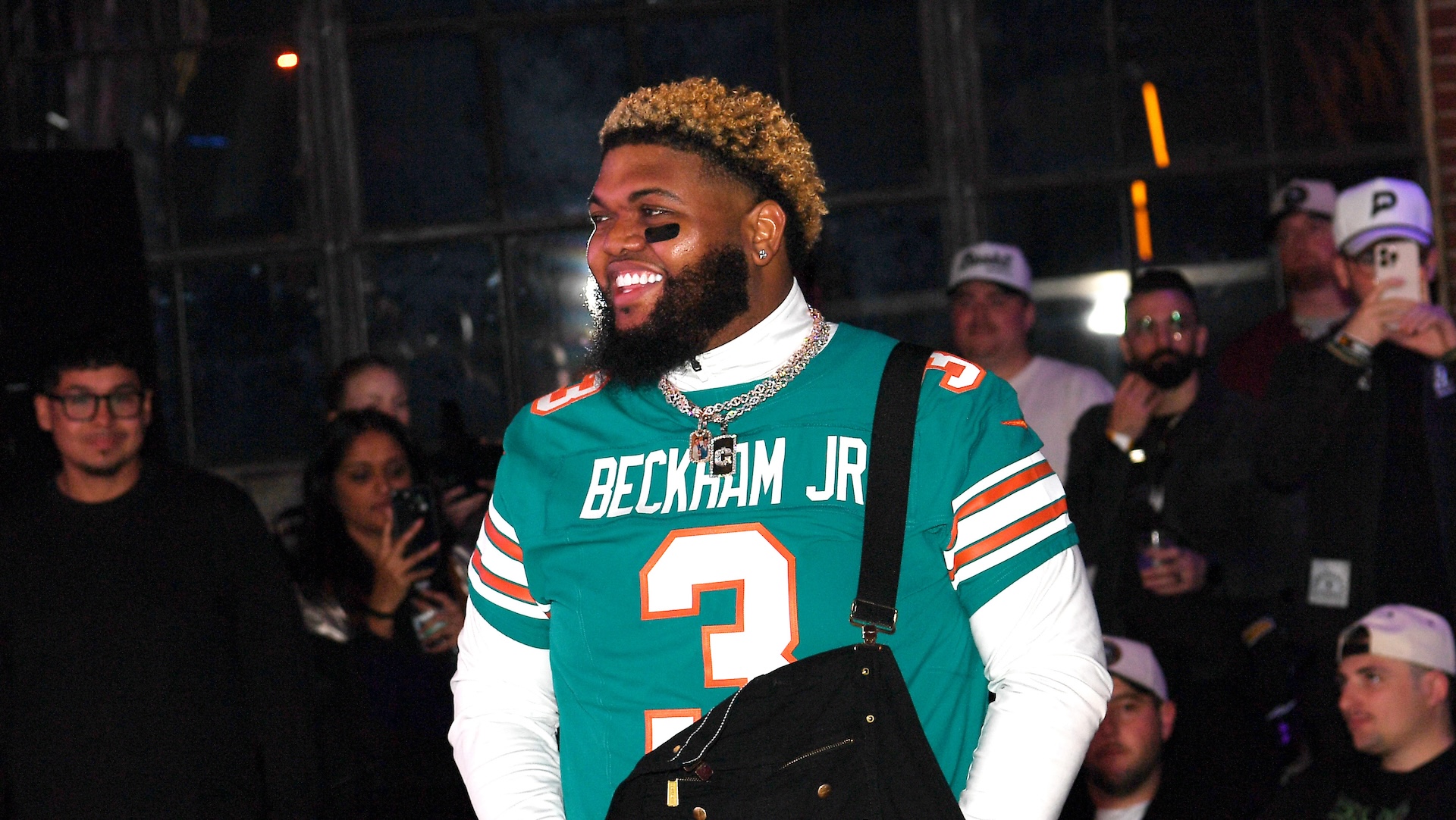 Druski wearing a "Beckham Jr" jersey with number 3, smiling at an event with a crowd in the background.