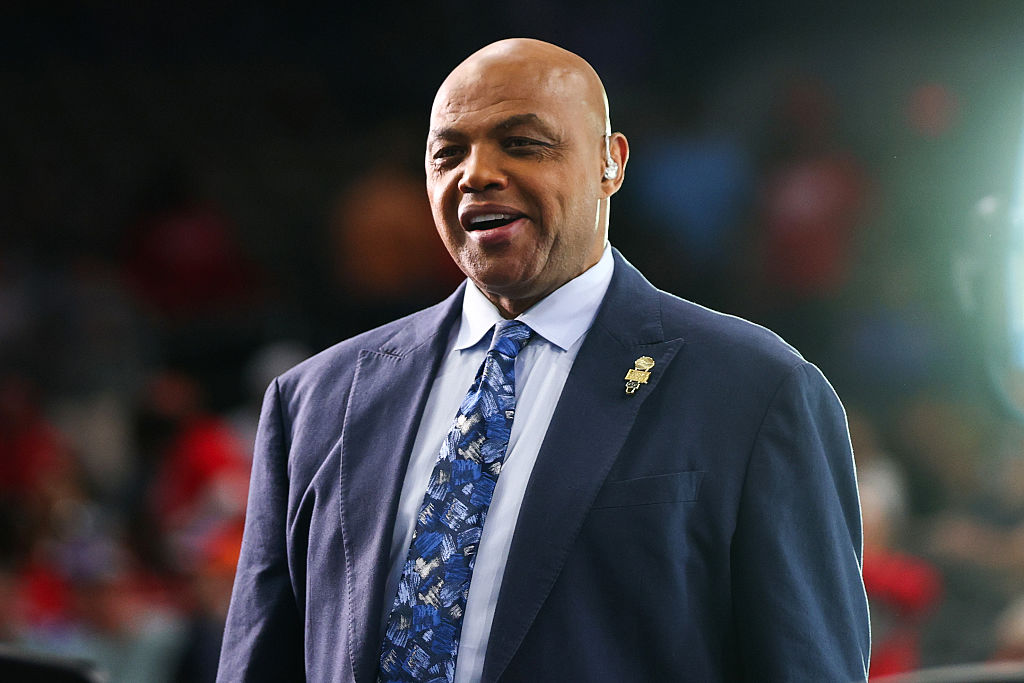Charles Barkley in a suit and tie, smiling, with a pin on his lapel.