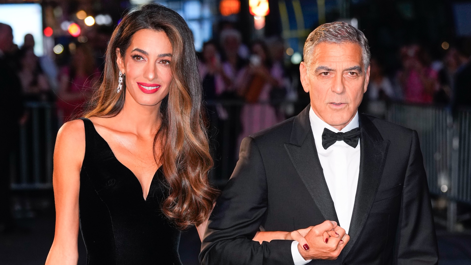 Amal Clooney in a black dress and George Clooney in a tuxedo, walking together at an event.