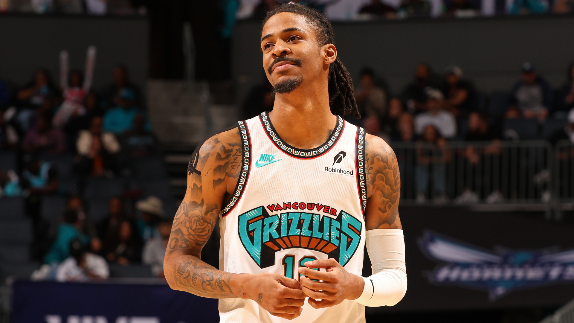 Ja Morant wearing a Vancouver Grizzlies jersey stands on the court, with tattoos on his arms and a focused expression.
