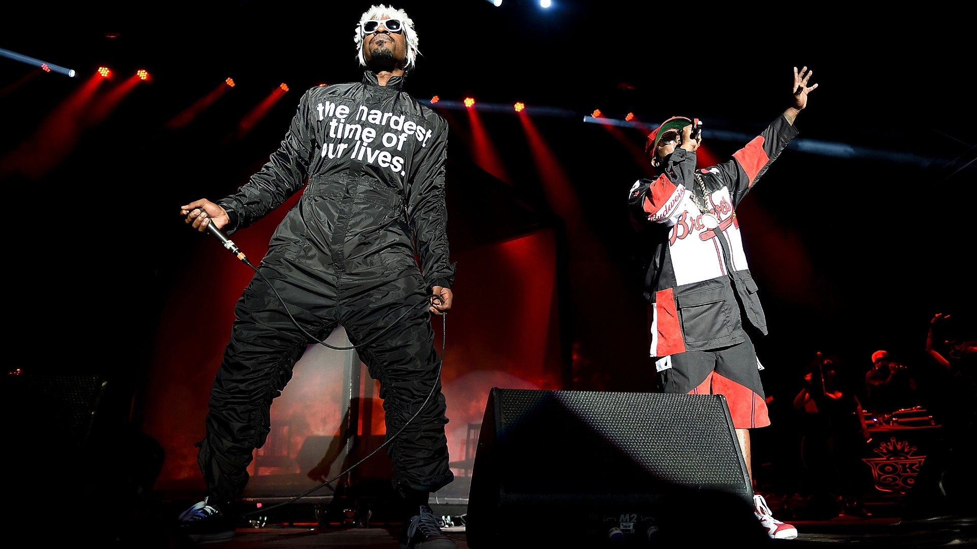 André 3000 and Big Boi performing on stage as OutKast, wearing distinctive outfits under bright stage lights.