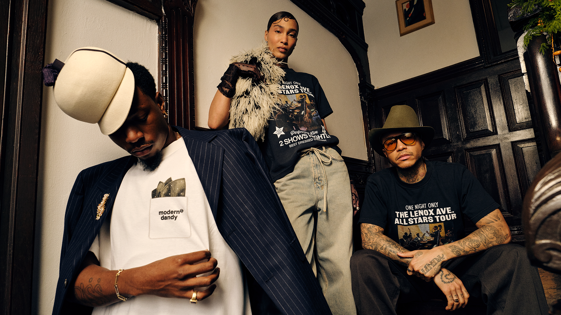 Three stylish individuals pose indoors, wearing hats and casual clothing with graphic prints, in a vintage setting.
