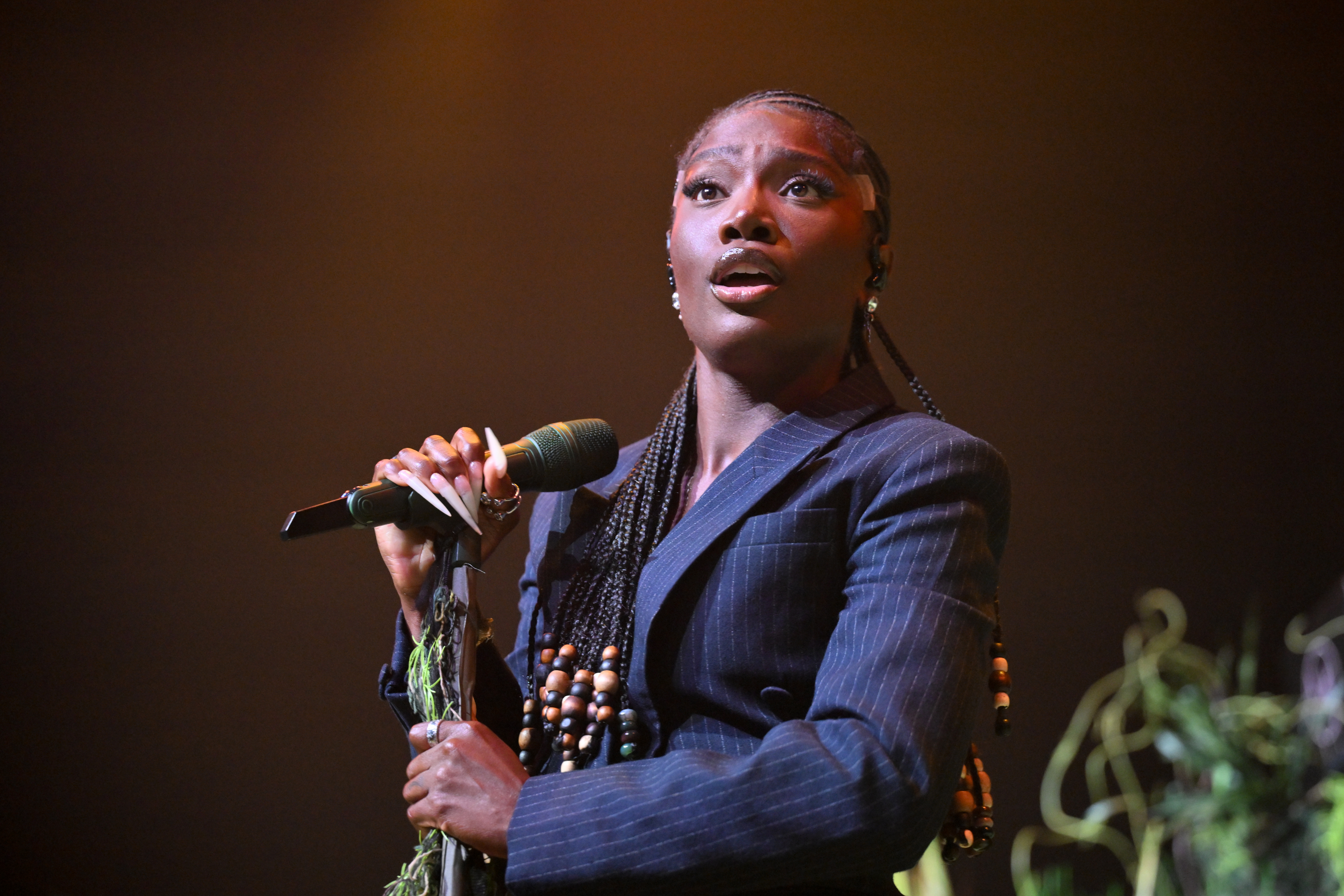 Doechii holding a mic wearing a big black suit.