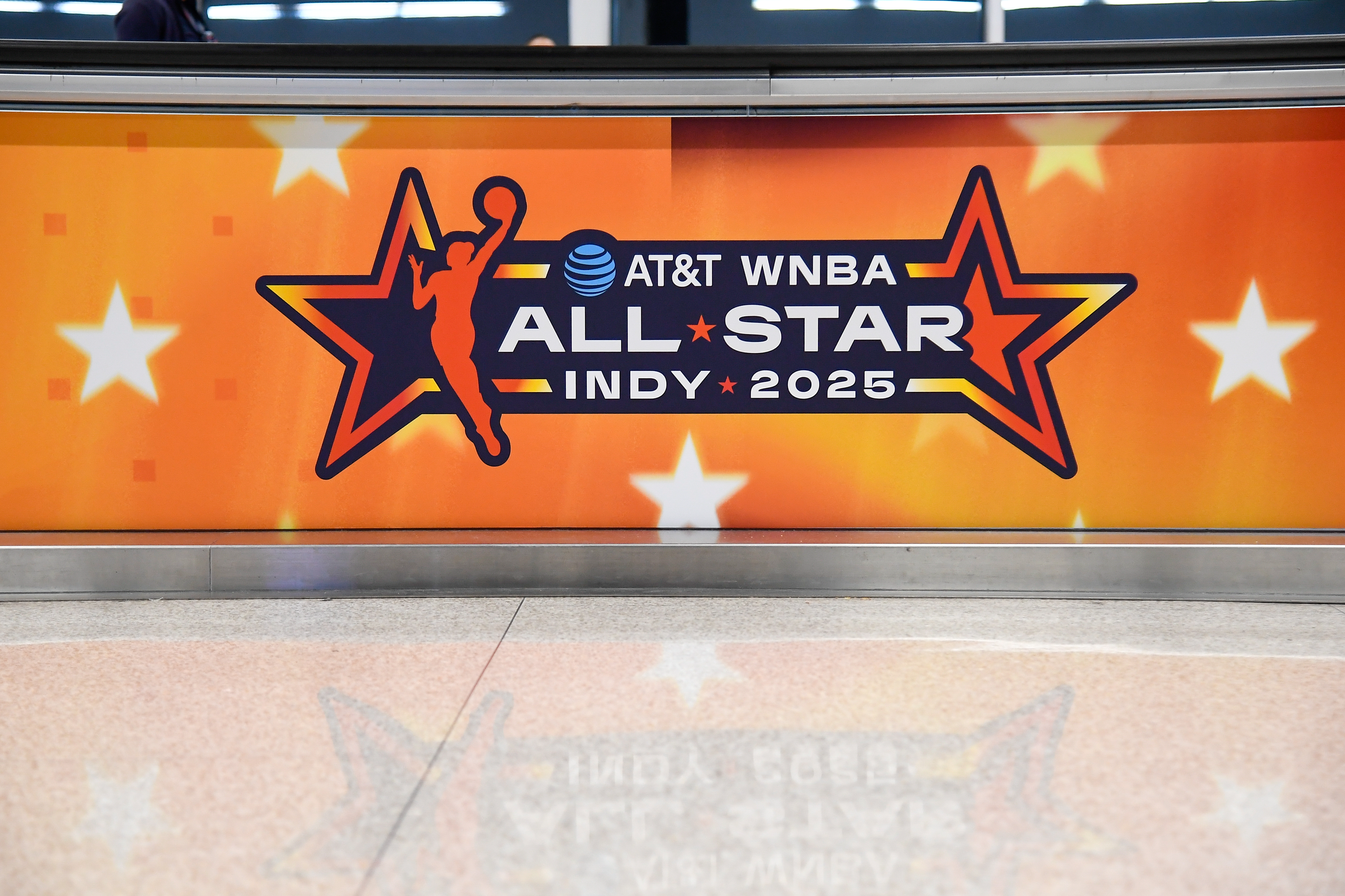 Sign for the AT&T WNBA All-Star Indy 2025 event, featuring a basketball player silhouette and star motifs on an orange background.