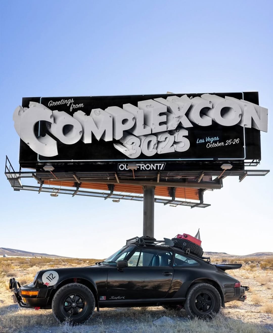 A black vintage Porsche with luggage on top is parked under a billboard for "ComplexCon 3025" in Las Vegas, October 25-26.