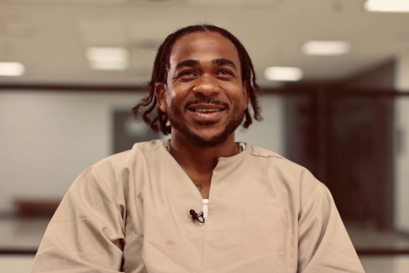 Max B with braided hair wearing a beige shirt, smiling in an indoor setting.