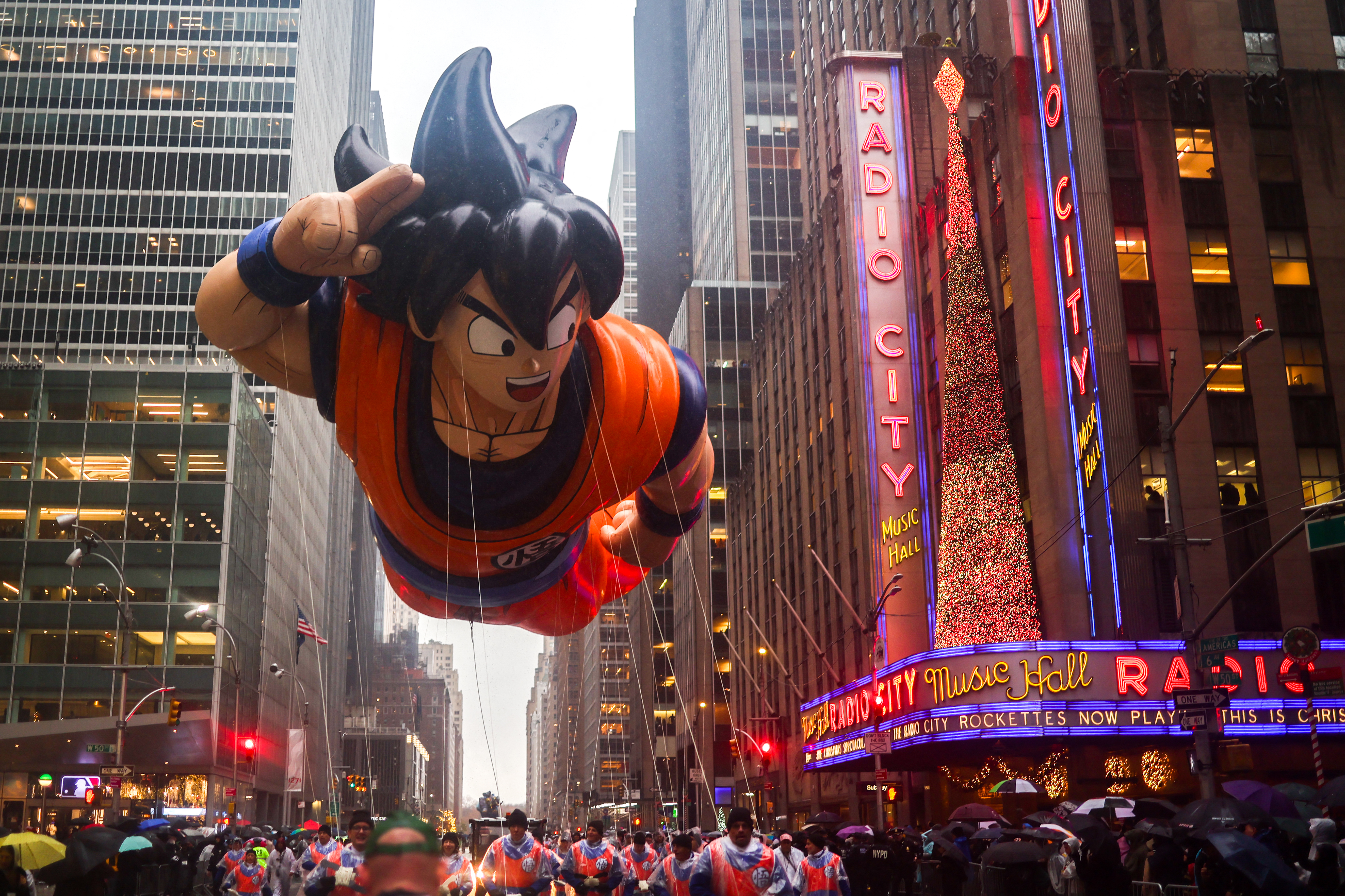 Giant Goku balloon from Dragon Ball in a parade near Radio City Music Hall, surrounded by buildings and spectators.