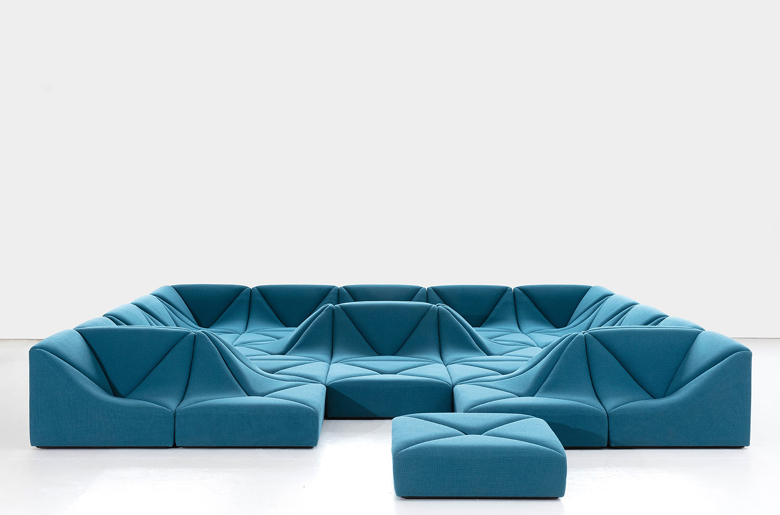 A modular, geometric teal sofa set with an ottoman on a white floor against a plain background.