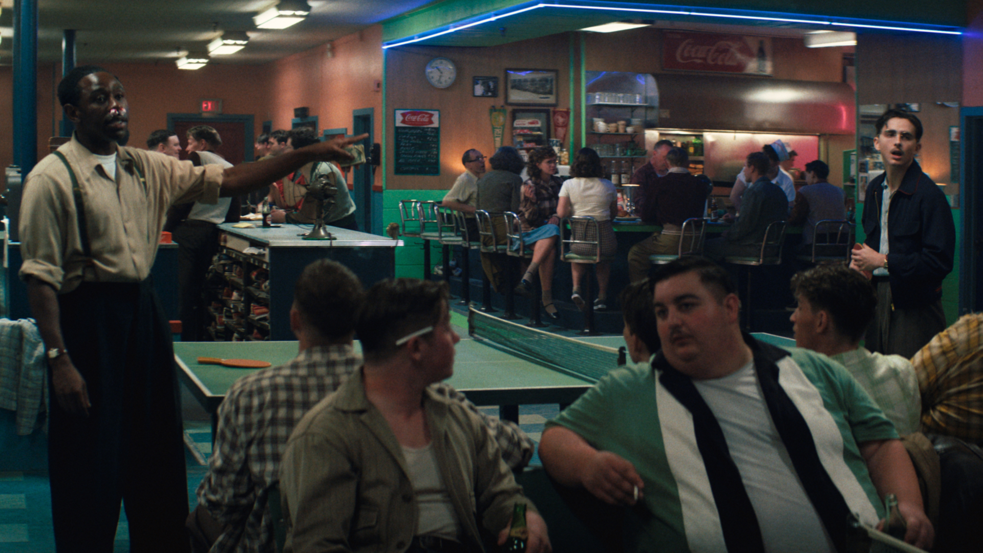 A retro diner scene with people sitting at a counter and tables. The atmosphere is lively with vintage decor and lighting.