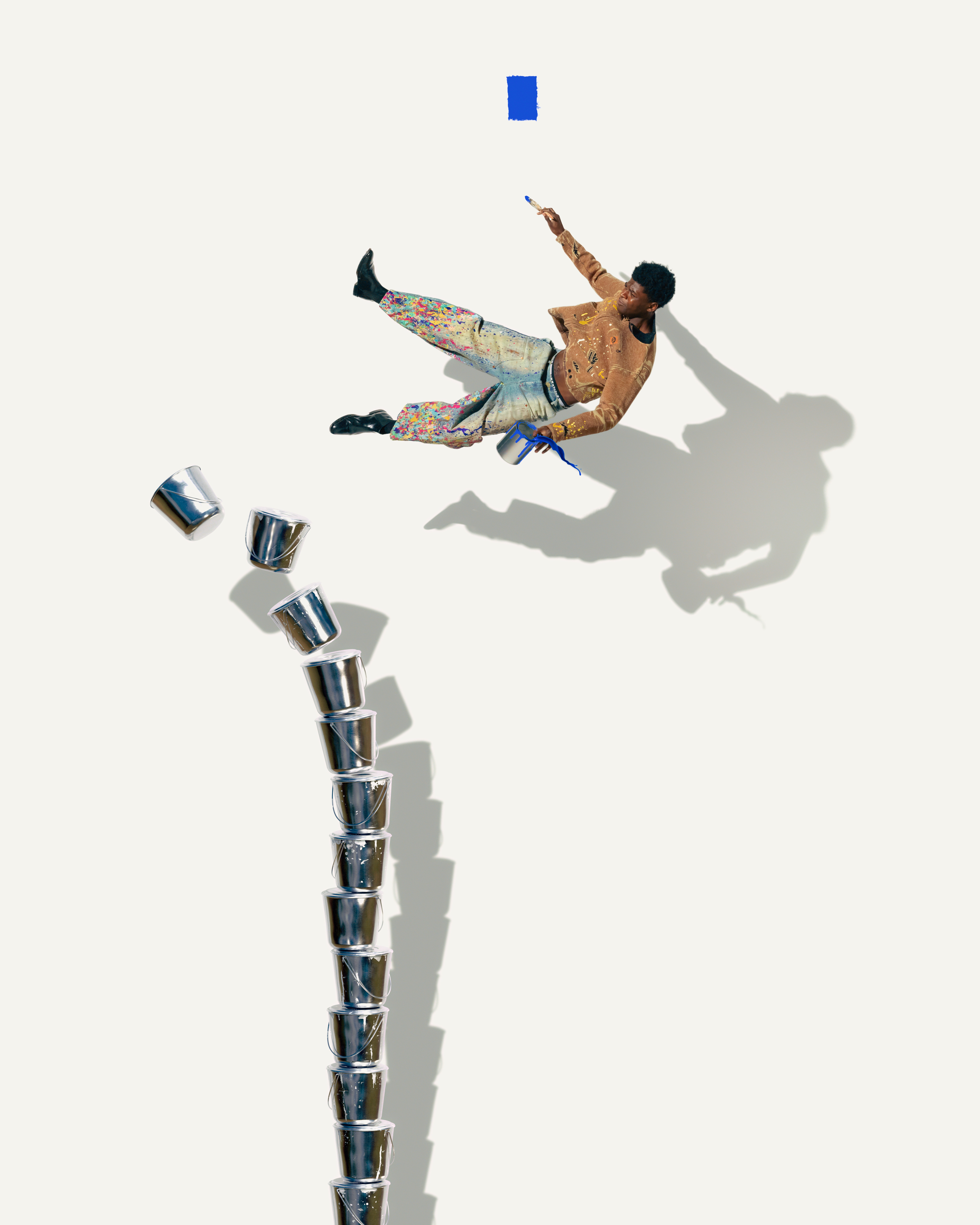 A person in colorful clothing appears to be floating, holding a paintbrush near a blue square, with a stack of metal buckets below.
