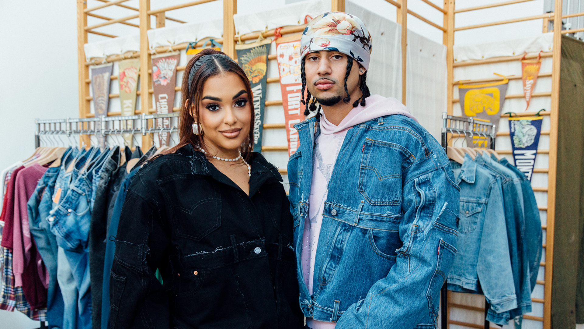 A woman and a man in a clothing store, both wearing denim jackets. The woman has long hair, and the man wears a patterned headscarf.
