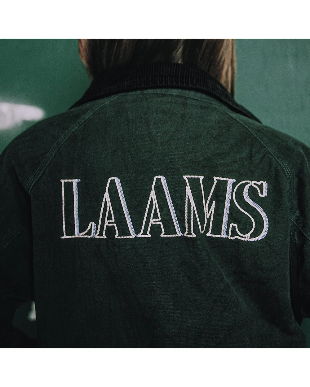 A person wearing a dark jacket with "LAAMS" embroidered on the back.