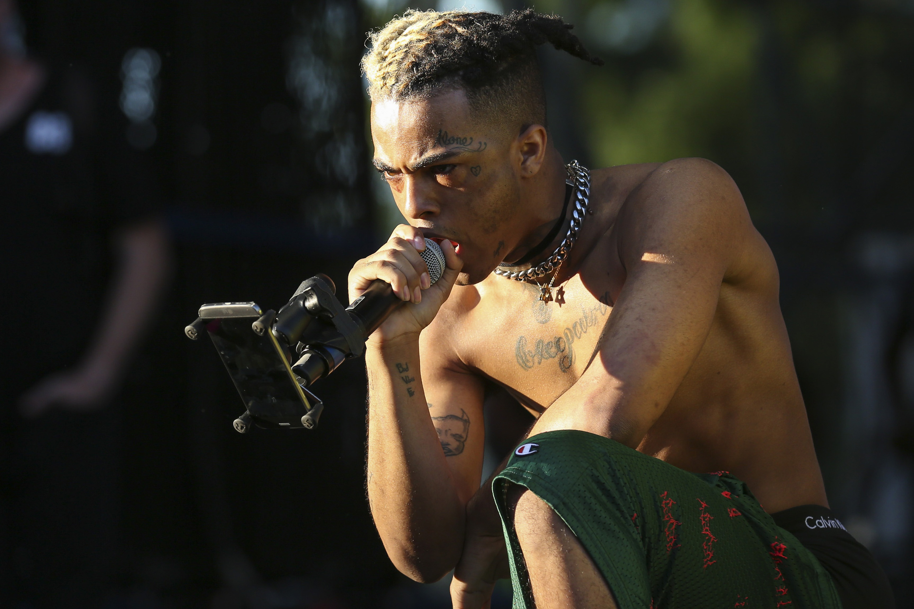 XXXTENTACION, who is shirtless, with tattoos and braided hair passionately singing into a microphone on stage. This is a list of things people didn't know about the rapper.