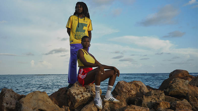 Two people in colorful athletic wear pose on rocks by the sea under a cloudy sky.