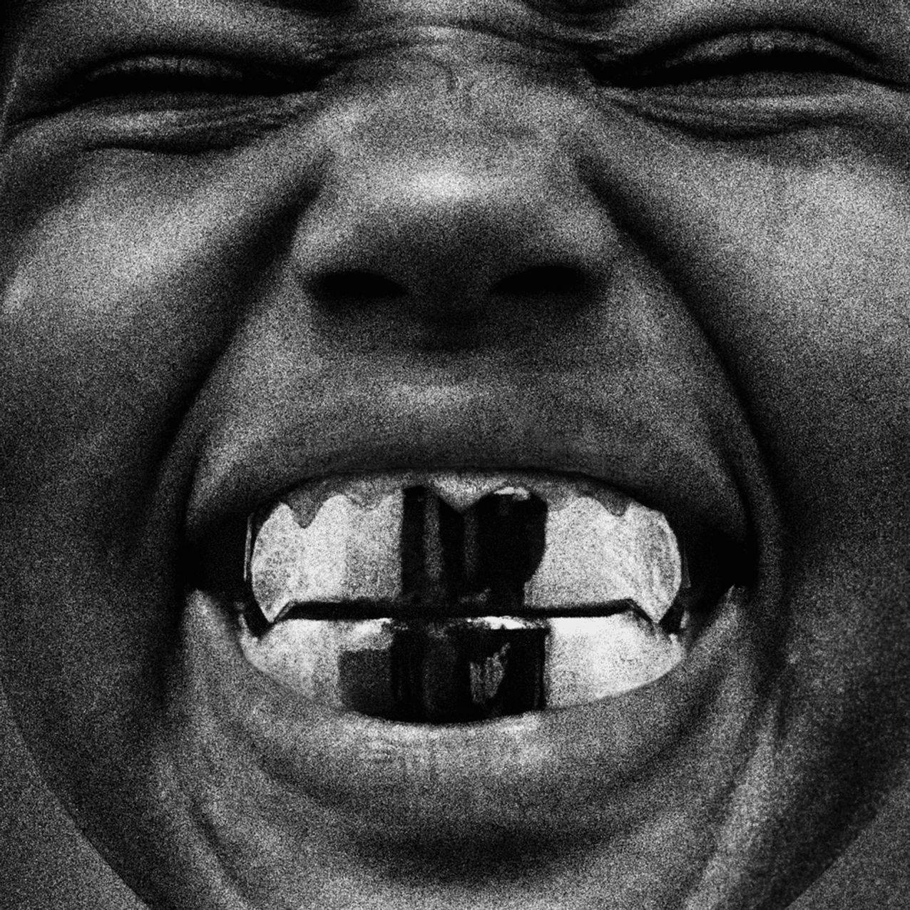 A close-up black and white image of Kanye West's son smiling with metallic dental grills. The eyes are closed, and the expression is joyful.