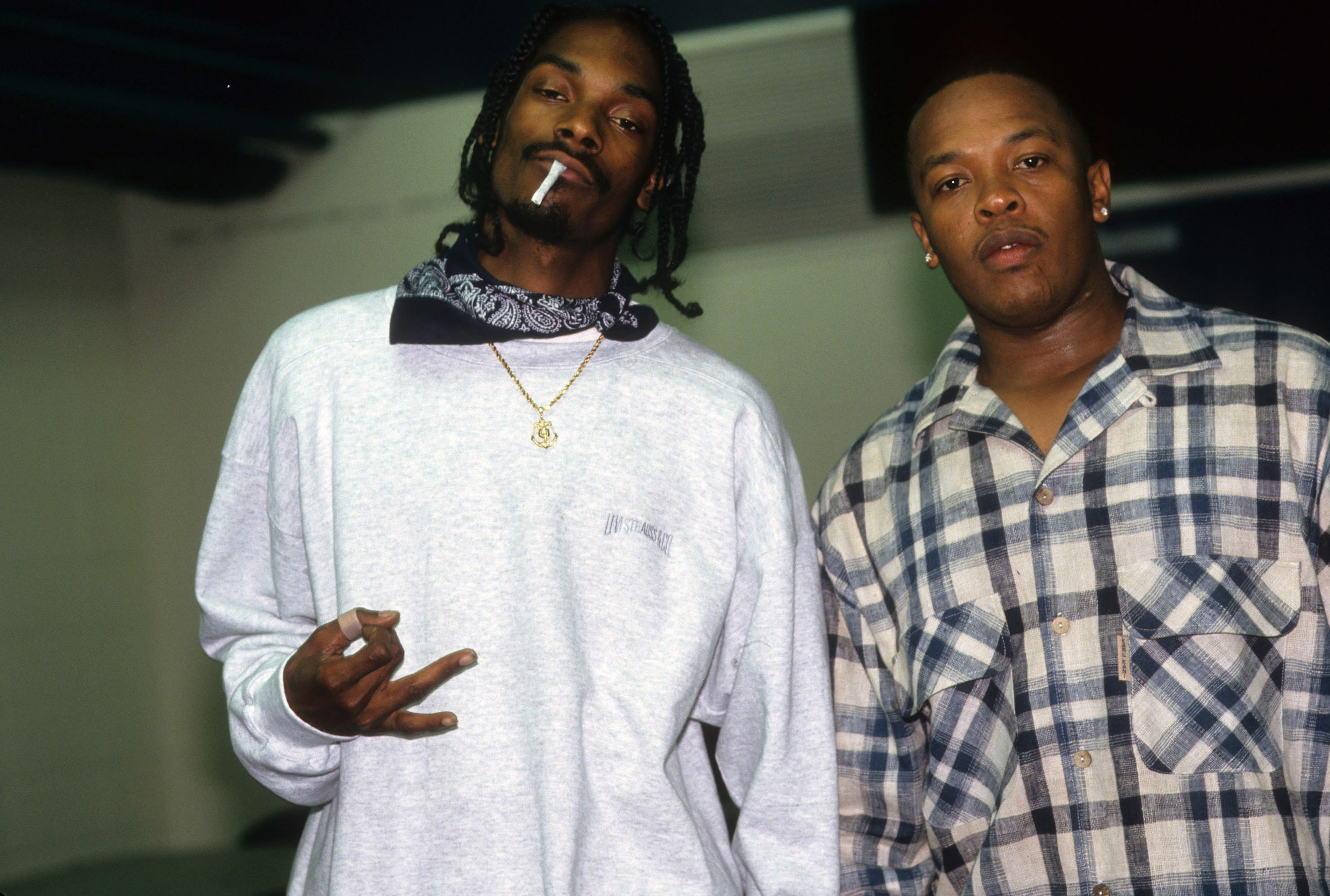 Snoop Dogg on stage, wearing sunglasses and a patterned shirt, smoking with a relaxed expression. The two are 4/20 legends with all the weed anthems they made. 
