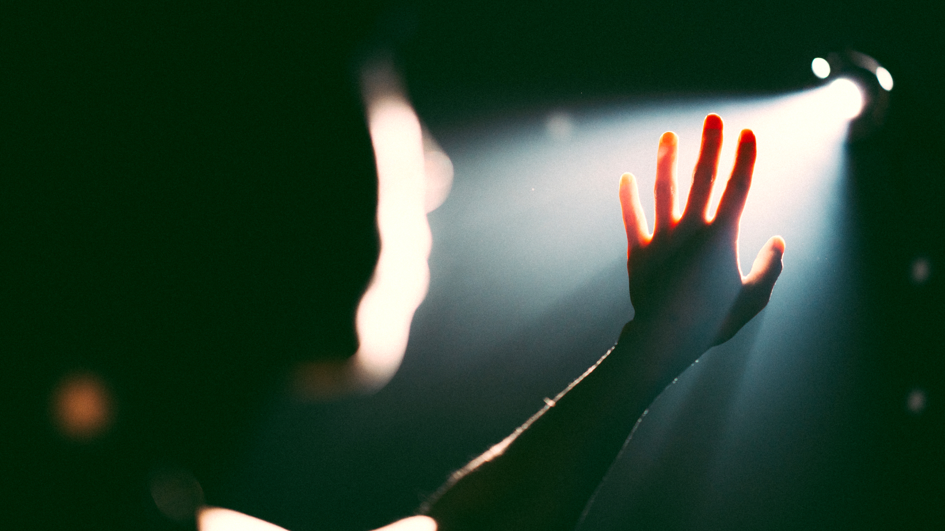 A hand reaching towards a bright light in a dark setting, with the figure's silhouette partially visible.