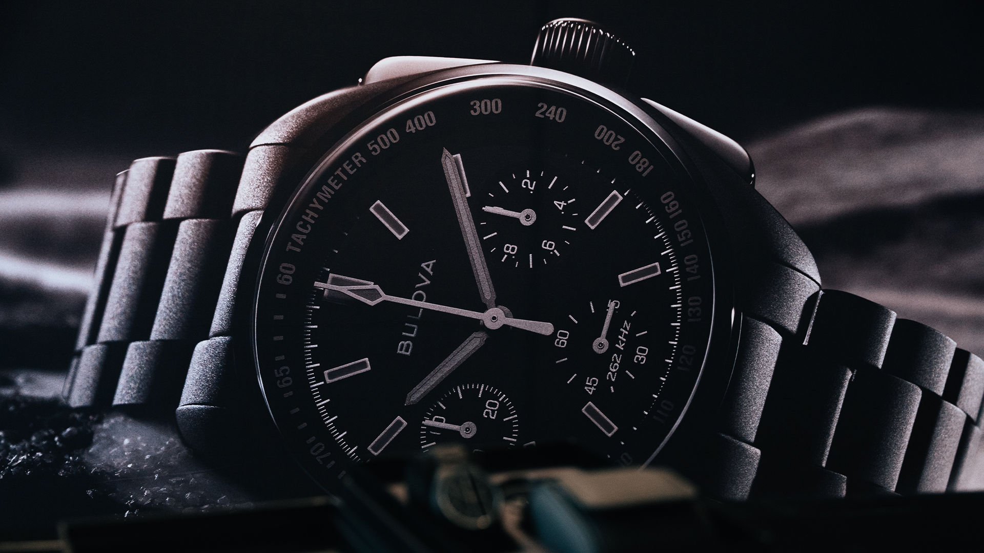 A close-up of a Bulova chronograph watch with a metal bracelet, featuring multiple subdials and a tachymeter on the bezel.