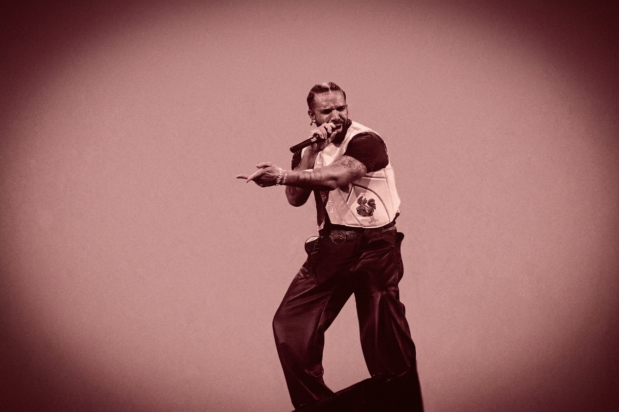 Drake on stage, holding a microphone, wearing a vest and pants. The image has a sepia tone, creating a vintage effect.