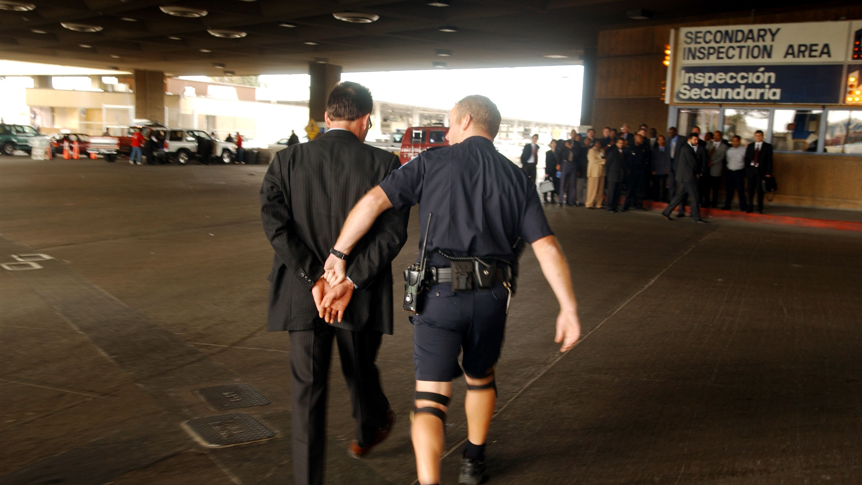 SAN YSIDRO, CA - FEBRUARY 24: A man is led away in handcuffs by a U.S. Customs inspector after a drug-sniffing dog found what inspectors believe to be marijuana hidden in the pane