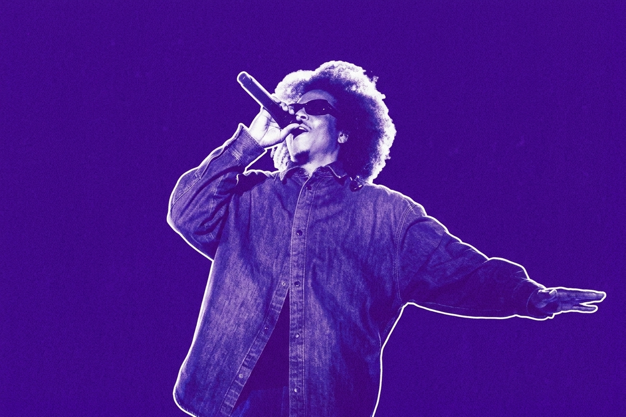 Jay-Z with an afro hairstyle and sunglasses sings passionately into a microphone, wearing a denim shirt, against a purple background. This is a photo from Roots Picnic 2026