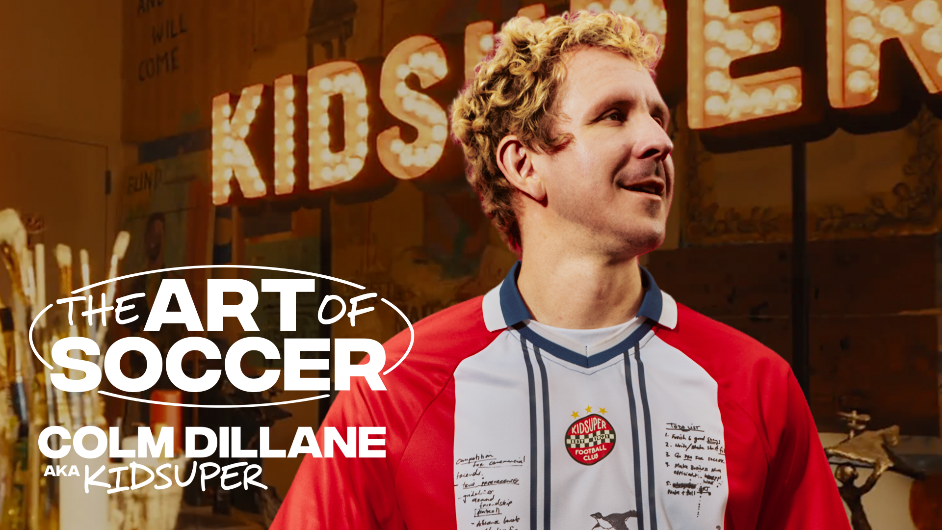 Colm Dillane, aka KidSuper, in a red and white soccer jersey, with "The Art of Soccer" text in the background.
